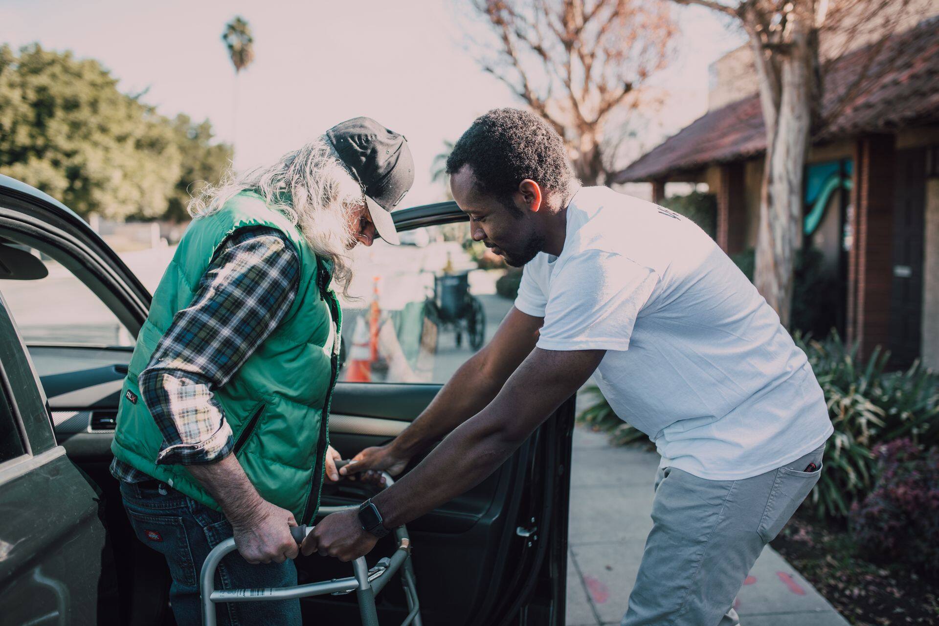 A volunteer helping an older man walk to his car